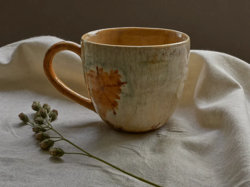 Tazza ceramica smaltata a mano su tessuto di lino accanto a fiori secchi
