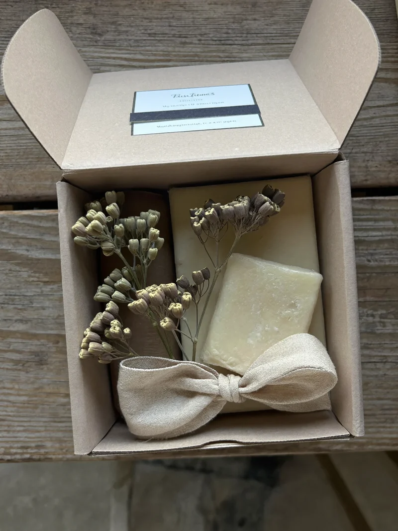 Scatola kraft aperta con botanici essiccati, dolci artigianali e nastro di lino